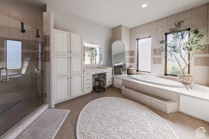 Tile flooring and walls, a glass-enclosed shower, a built-in soaking tub, a vanity with integrated lighting, and extensive cabinetry