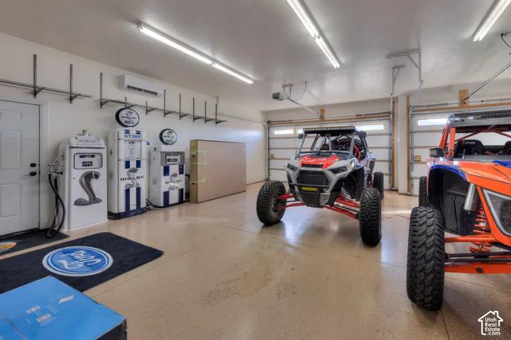 Epoxy flooring, multiple overhead fluorescent light fixtures, two roll-up garage doors, wall-mounted shelving, and a mini-split system