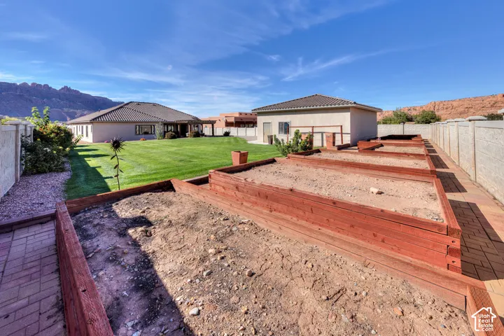 Manicured lawn, multiple raised garden beds, brick paver hardscaping, stucco exterior, and a tile roof