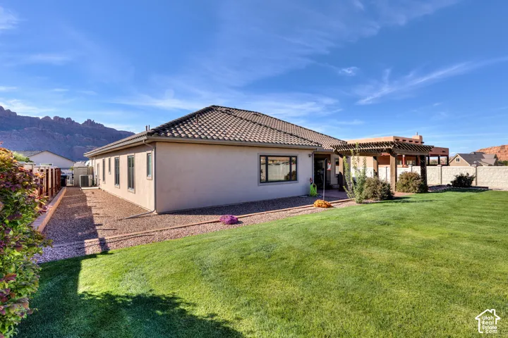 Expansive lawn with a tiled roof residence, a pergola-covered patio, and a gravel-lined side yard