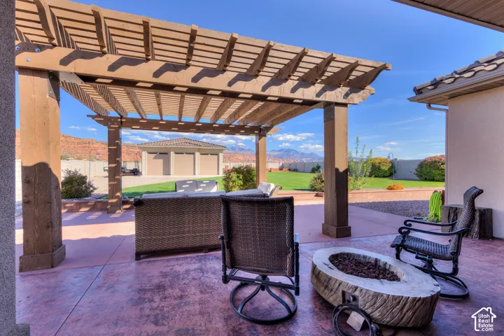 Covered patio with a wood pergola, stamped concrete flooring, and a built-in fire pit