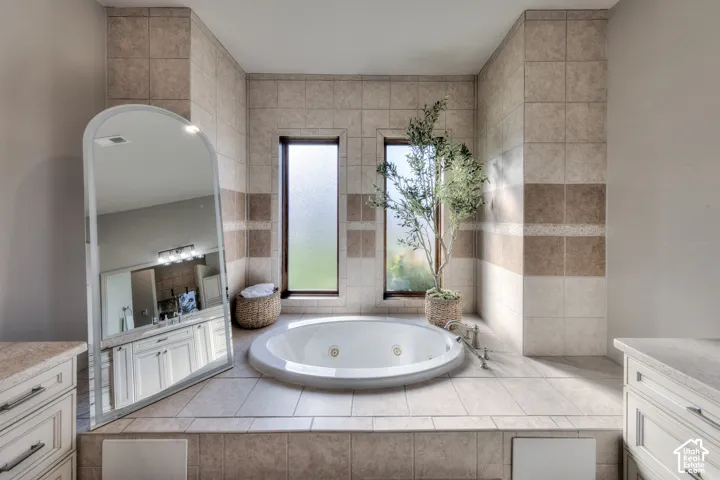Built-in jetted tub surrounded by tile, dual vertical windows with privacy glass, and matching tile accent bands