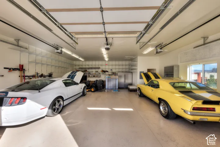 Spacious garage featuring a durable epoxy floor, extensive built-in shelving, abundant overhead fluorescent lighting, and large windows