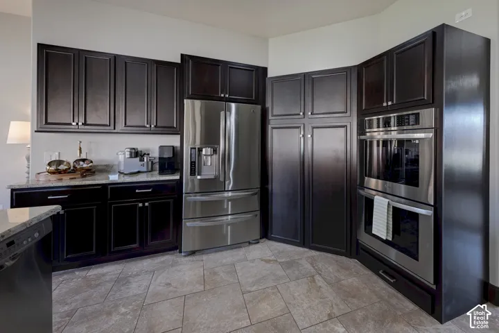 Dark wood-finish cabinetry with silver hardware, stainless steel refrigerator, stainless steel double ovens, light-toned countertop, and tiled flooring
