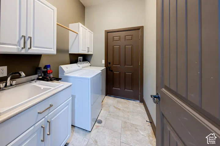 Laundry area featuring white cabinetry with silver hardware, a utility sink with a chrome faucet, and tiled flooring