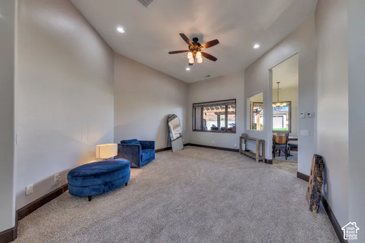 Carpeted living area featuring a ceiling fan with integrated lighting, recessed lighting, and a large window with dark wood trim