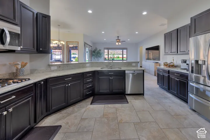 Kitchen featuring stainless steel appliances, dark wood cabinetry, light stone countertops, a gas cooktop, and neutral tile flooring