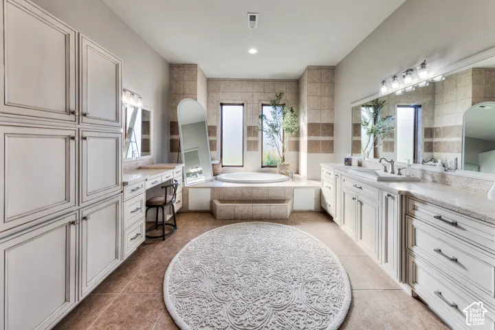 Built-in cabinetry, dual vanities with integrated sinks, jetted soaking tub, tiled flooring, and multiple windows