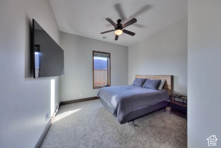 Wall-mounted display, recessed window with wood trim, ceiling fan with integrated lighting, and carpeted flooring
