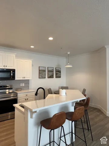 White shaker-style cabinetry with dark hardware, stainless steel appliances, a black gooseneck faucet, light-toned countertops, and wood-finish flooring