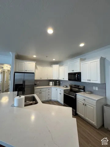 White cabinetry with dark hardware, stainless steel refrigerator, black range, and wood-finish flooring