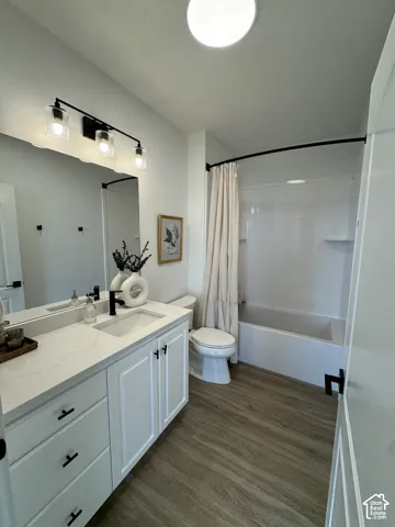 White vanity with black hardware, quartz countertop, undemount sink, wood-finish flooring, and a shower-tub combination