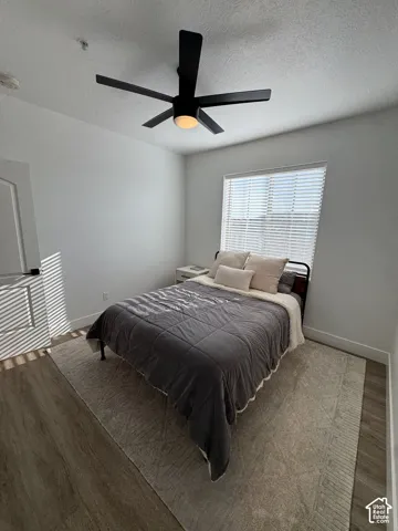 Wood-finish flooring, white walls, black ceiling fan with integrated lighting, and a window with horizontal blinds