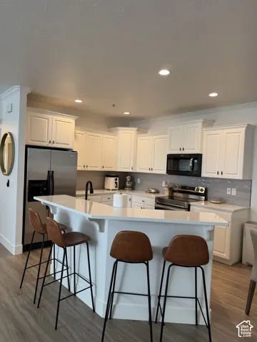 Kitchen featuring white cabinetry, stainless steel appliances, light-toned countertops, tile backsplash, and recessed lighting