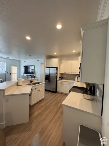White cabinetry, wood-finish flooring, recessed lighting, stainless steel appliances, and a tile backsplash