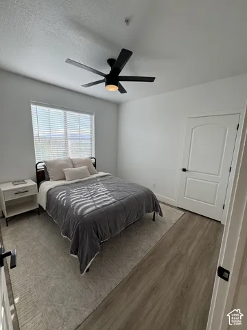White walls, wood-finish flooring, white window blinds, and a black ceiling fan with integrated lighting