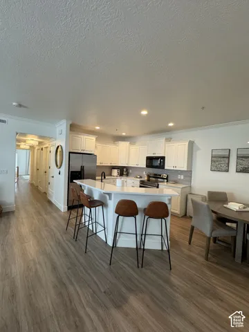 Open-concept kitchen featuring white cabinetry, stainless steel appliances, a center island with seating, and wood-finish flooring