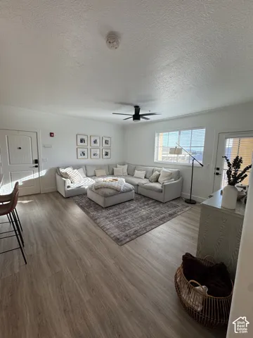 Wood-finish flooring throughout, featuring a ceiling fan with light, crown molding, and a visible window with horizontal blinds
