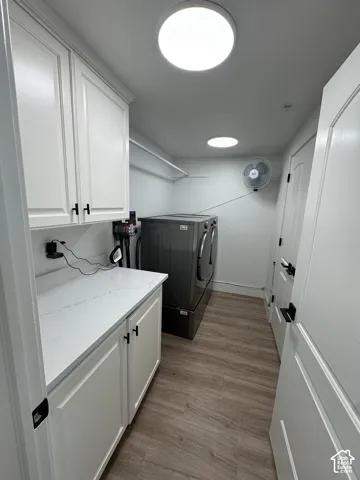 White shaker-style cabinetry with matte black hardware, white countertop, wood-finish flooring, and overhead lighting