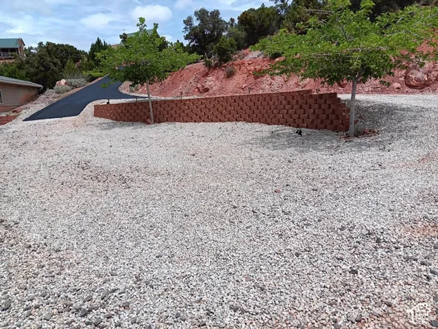 Gravel-covered terrain with a paved driveway, featuring a stacked block retaining wall