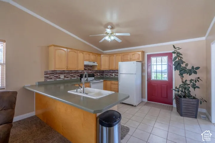 Vaulted ceiling with a ceiling fan, light wood-finish cabinetry, tile backsplash, kitchen island with integrated sink, and tile flooring