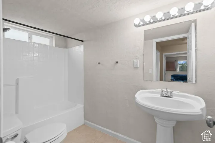 Pedestal sink with chrome faucet, integrated mirror with vanity lighting, and a white tiled shower/tub combination