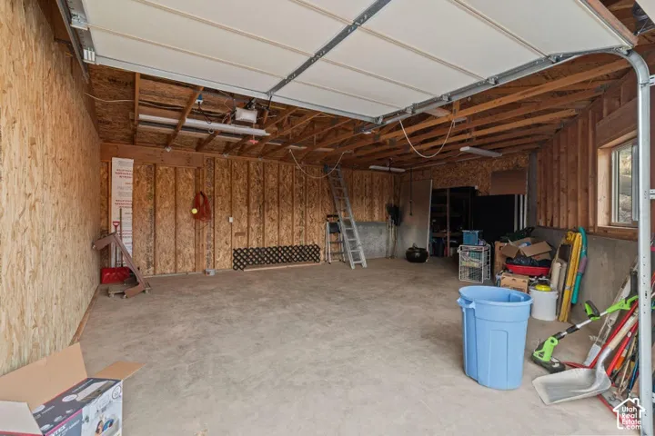 Attached garage with concrete flooring, wood-paneled walls, and exposed ceiling joists
