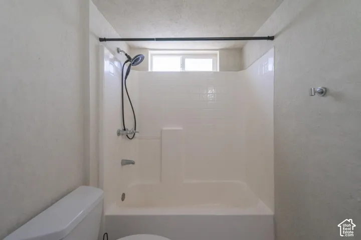 Bathtub with integrated shower, white tile surround, and a small window for natural light