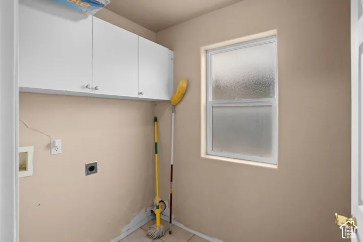 White upper cabinetry, single-hung window with privacy glass, wall-mounted electrical outlet, and utility hookups