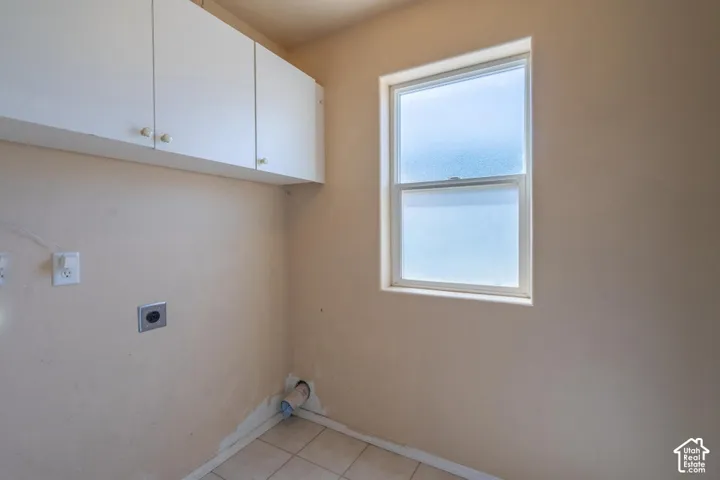 White cabinetry, frosted window, tile flooring, and utility hookups