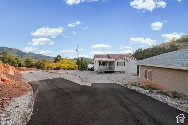 Paved driveway with gravel borders, leading to a residence with a red metal roof and an adjacent neutral-toned building