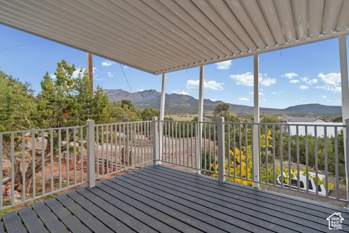 Covered outdoor deck with grey composite decking and a white metal railing, featuring a distant mountain backdrop