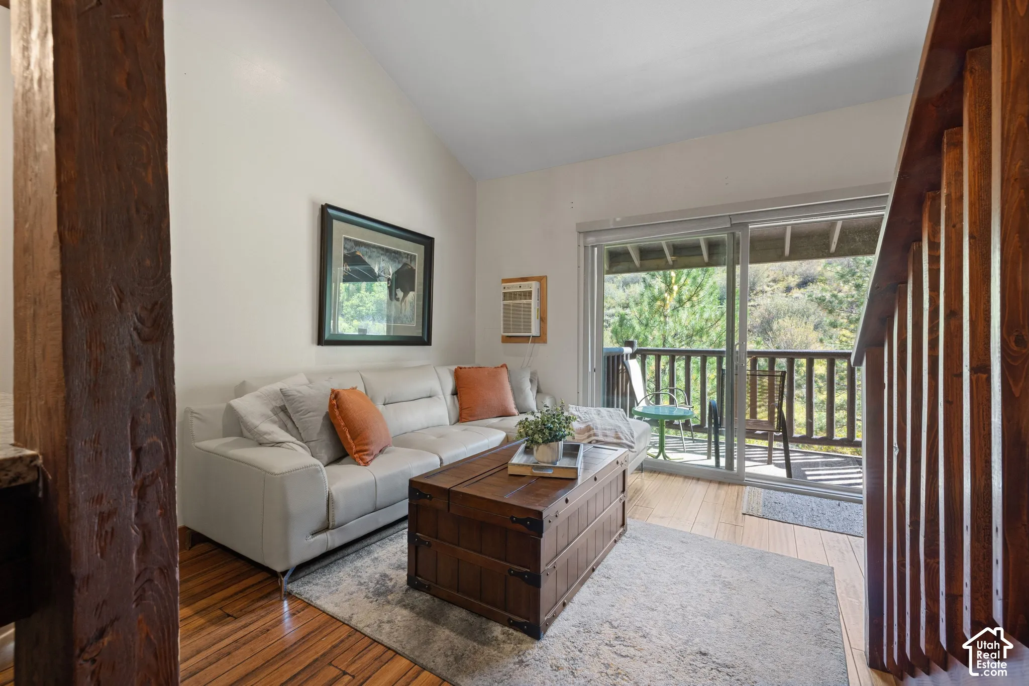 Sliding glass door leading to an outdoor balcony with wood railing, wood-finish flooring, and a vaulted ceiling