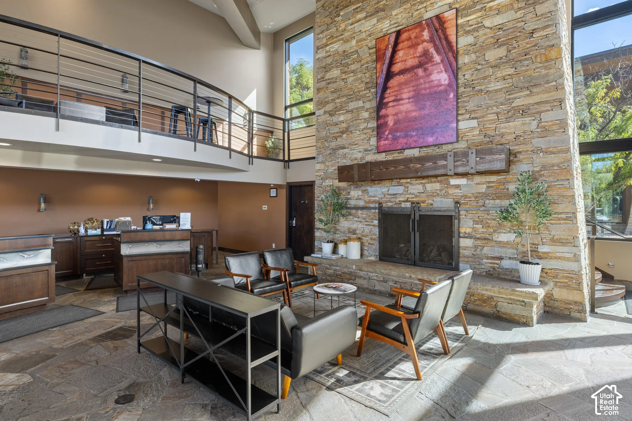 Stone-clad fireplace with hearth, two-story stone wall, floor-to-ceiling windows, and an open mezzanine with metal railings