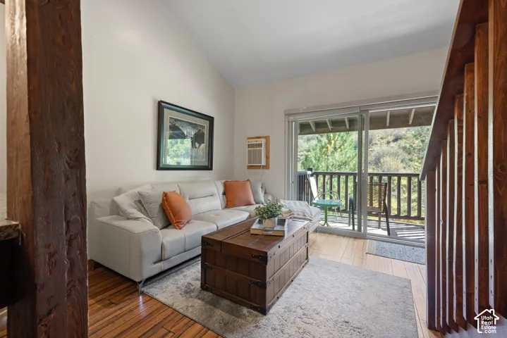 Sliding glass door leading to an outdoor balcony with wood railing, wood-finish flooring, and a vaulted ceiling