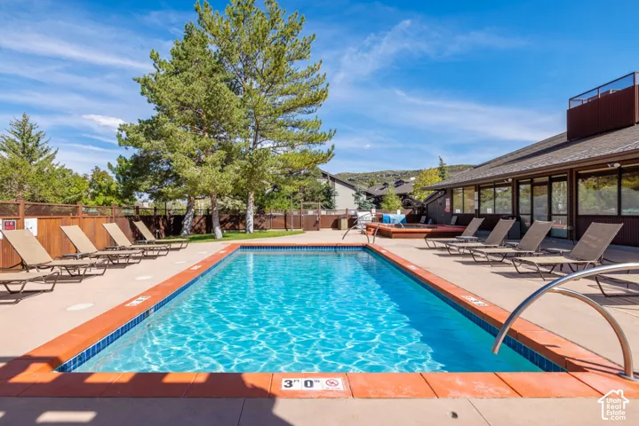 Rectangular swimming pool with a concrete surround, wood fencing, and mature trees