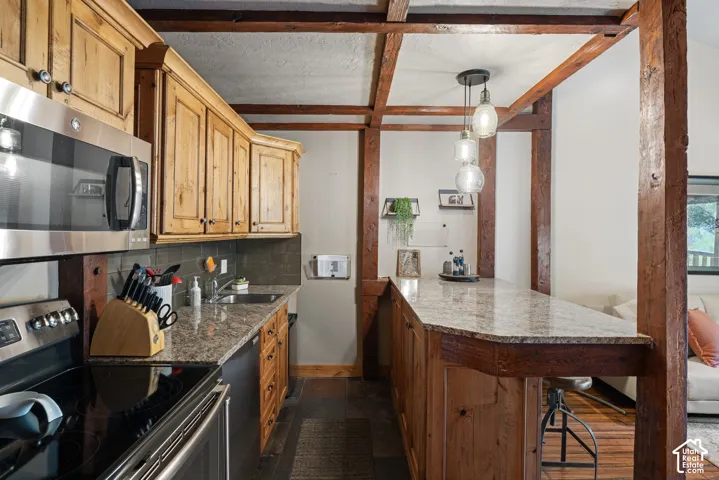 Kitchen featuring wood cabinetry, stainless steel appliances, a stone-finish countertop, and exposed timber beams
