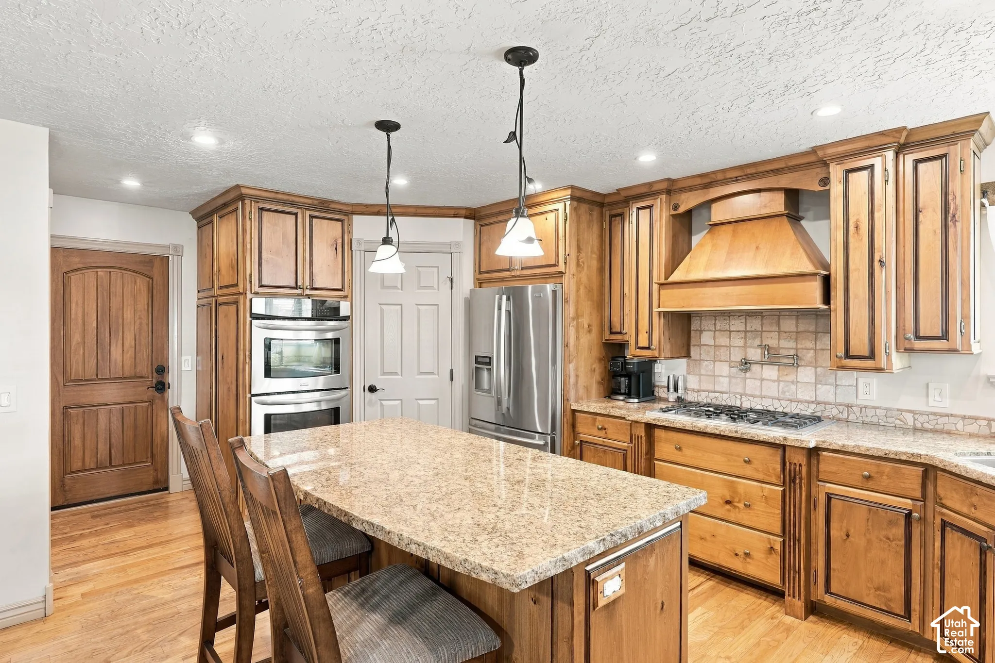Kitchen featuring wood-finish cabinetry, granite-finish countertops, stainless steel appliances, a center island with pendant lighting, and wood-finish flooring