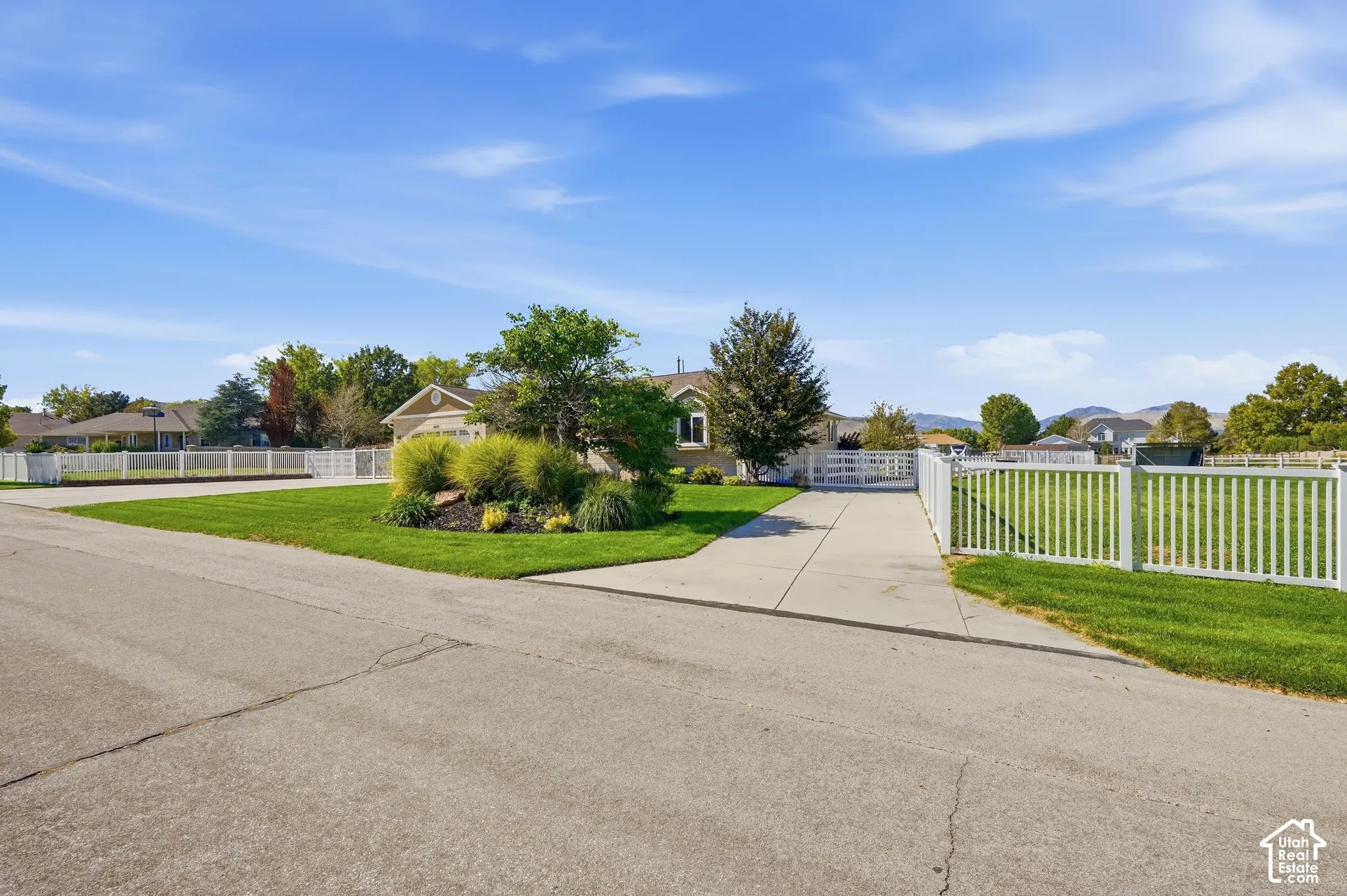 Expansive front yard with manicured lawn, white picket fencing, and a concrete driveway