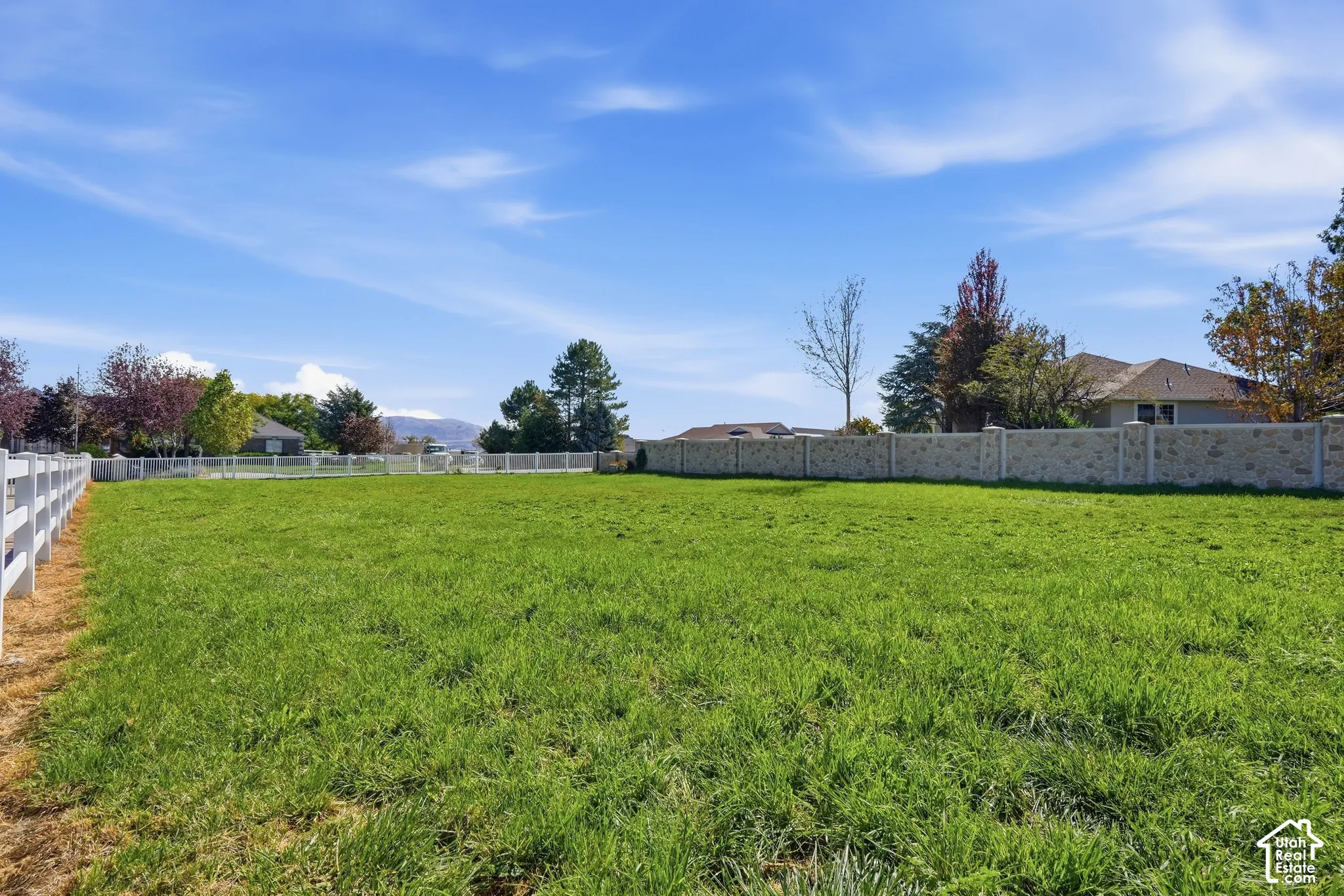Expansive parcel featuring a grassy field, white perimeter fencing, and a decorative stone wall