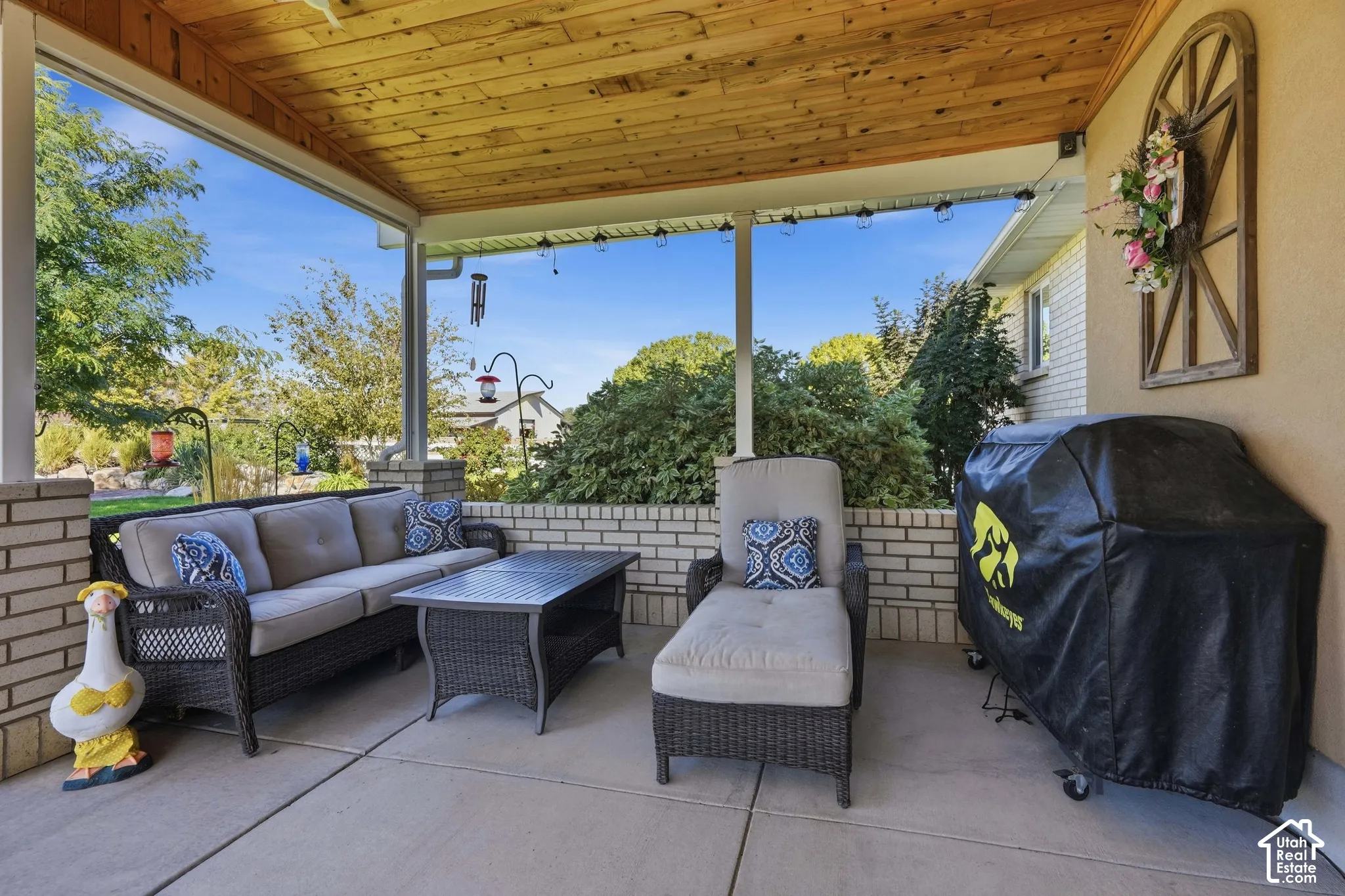 Covered patio featuring a wood-panel ceiling, concrete flooring, and brick half-walls
