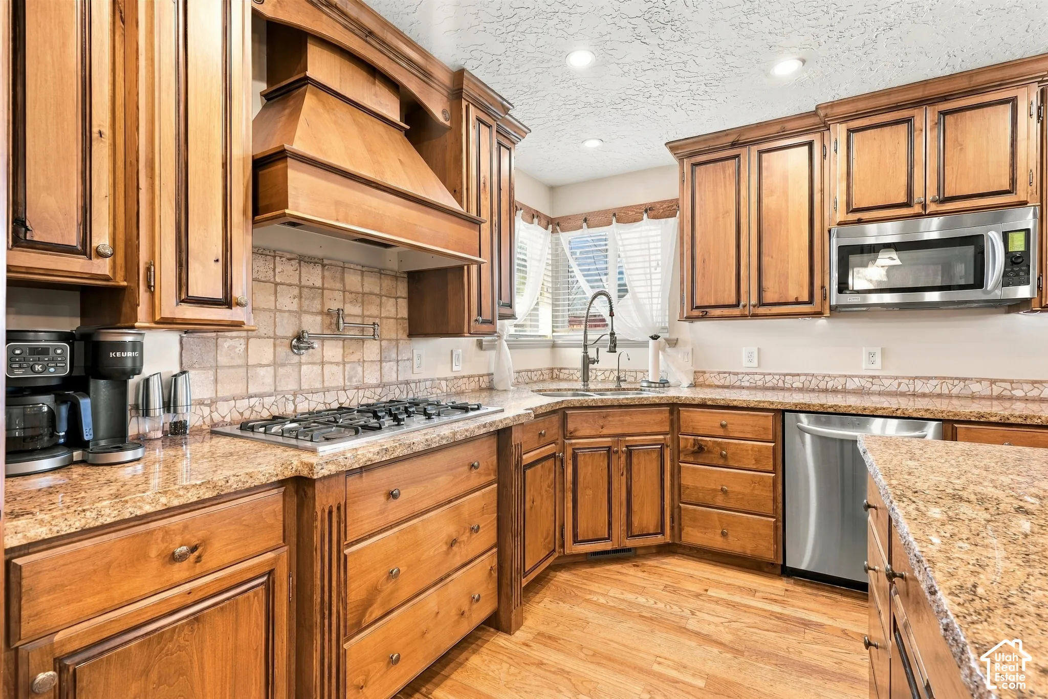 Wood-finish cabinetry, granite countertops, tile backsplash, stainless steel appliances, and wood-finish flooring