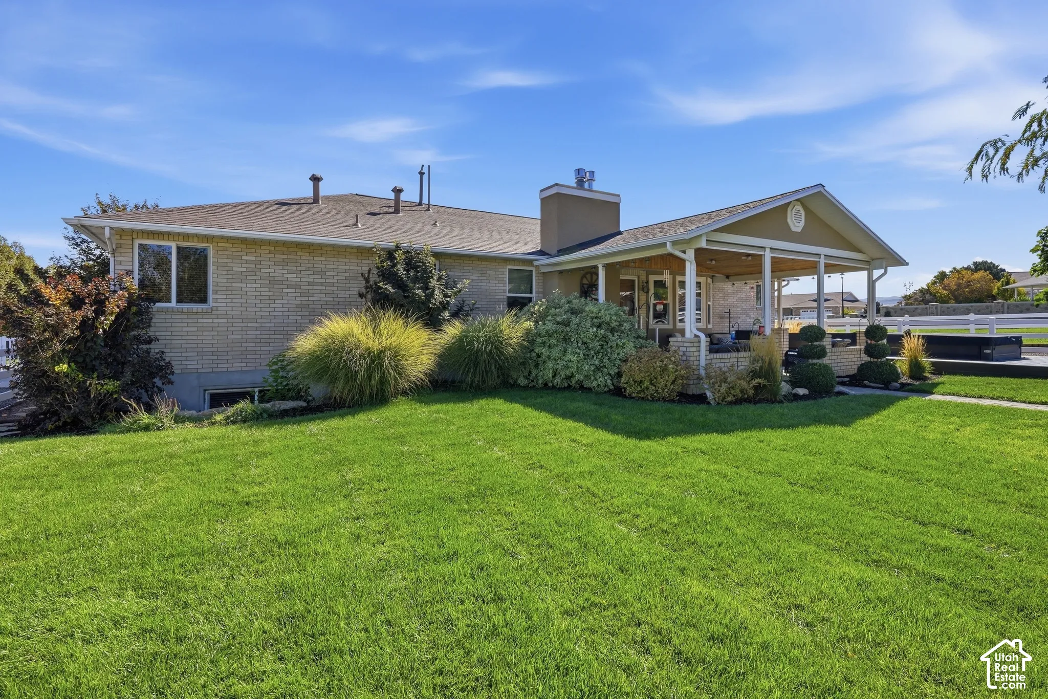 Expansive green lawn with mature landscaping, covered patio with white columns, and brick exterior