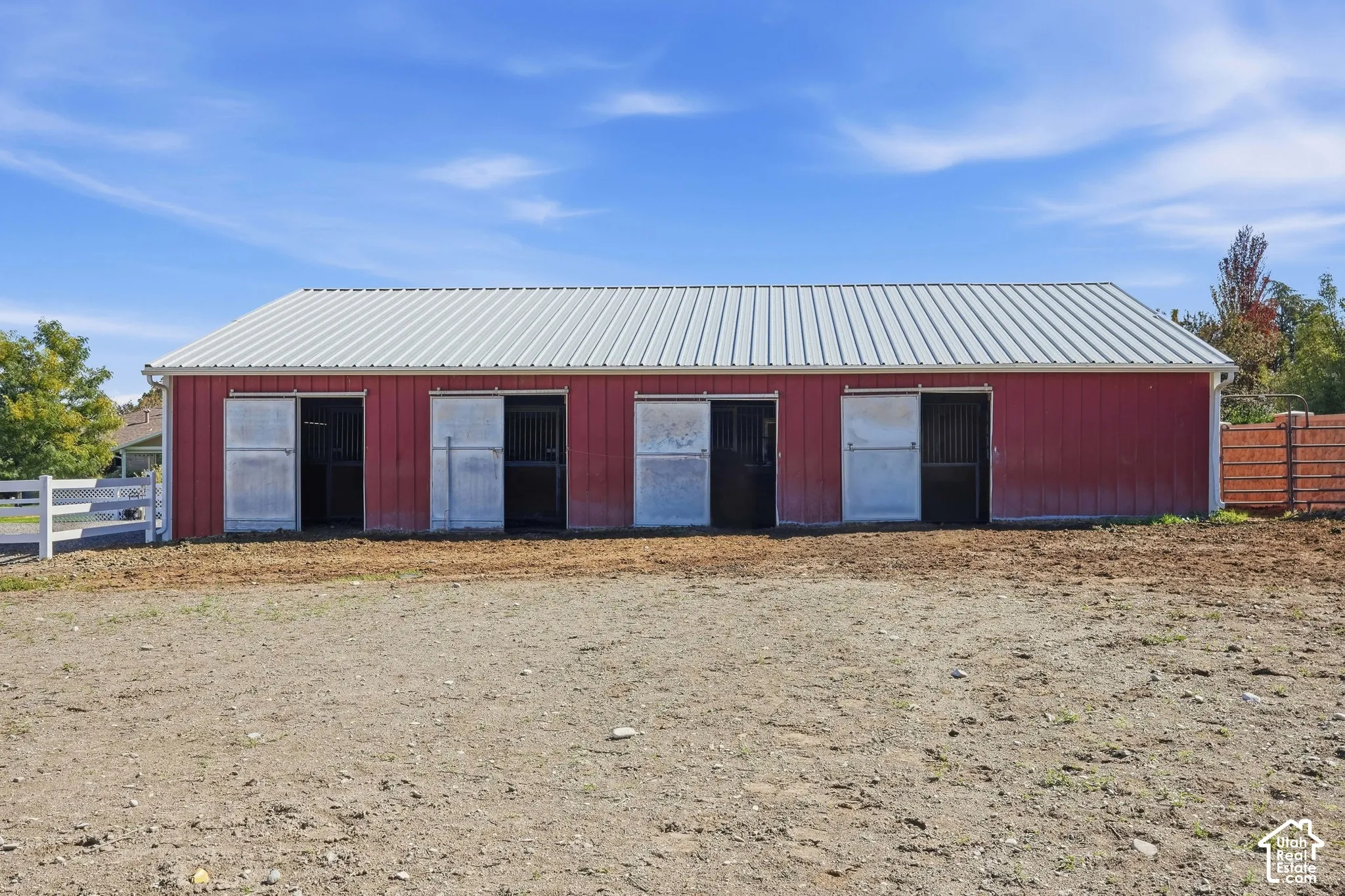 Red barn structure with a metal roof, five sliding doors, and white rain gutters