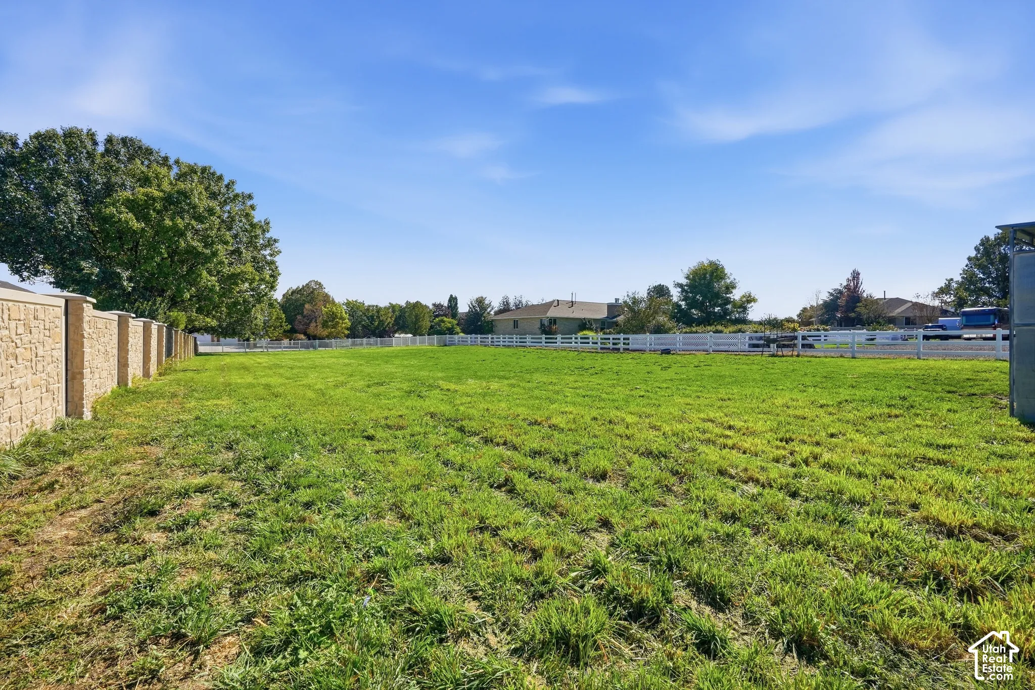 Expansive grassy lot, stone-clad perimeter wall, white rail fencing, mature trees