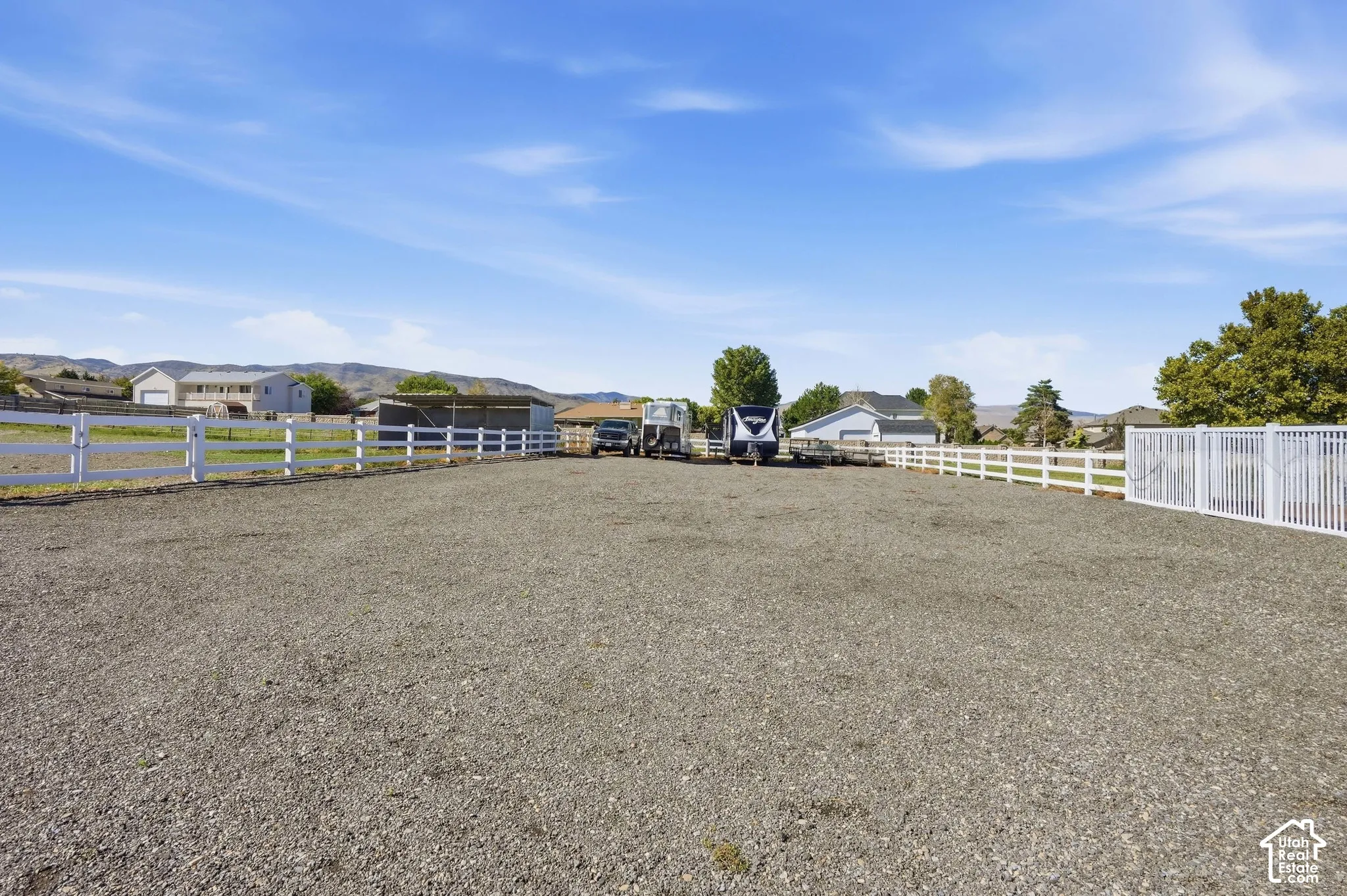 Expansive gravel area with white fencing and a metal outbuilding