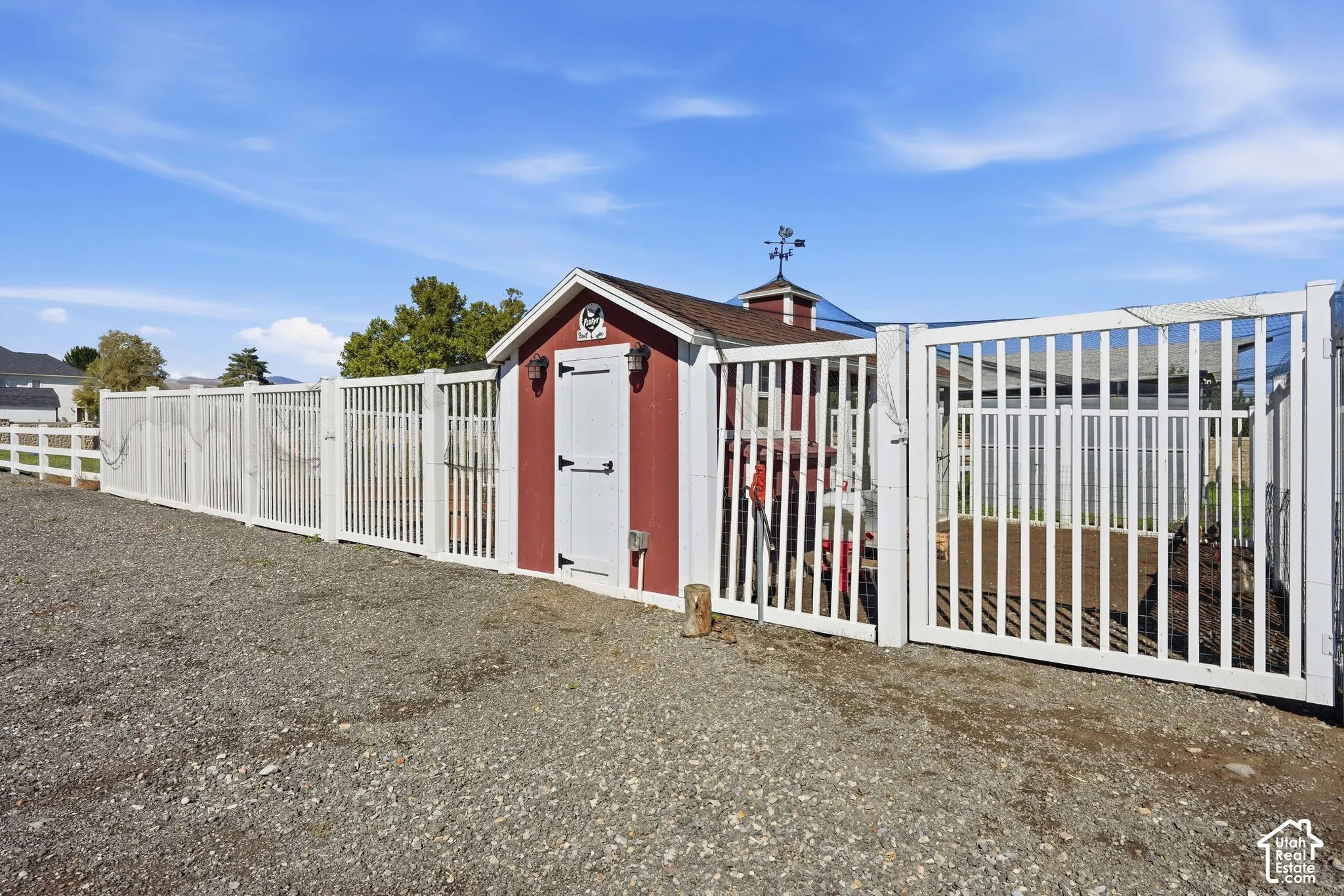 Red and white shed with a cupola and weathervane, bordered by a white picket fence