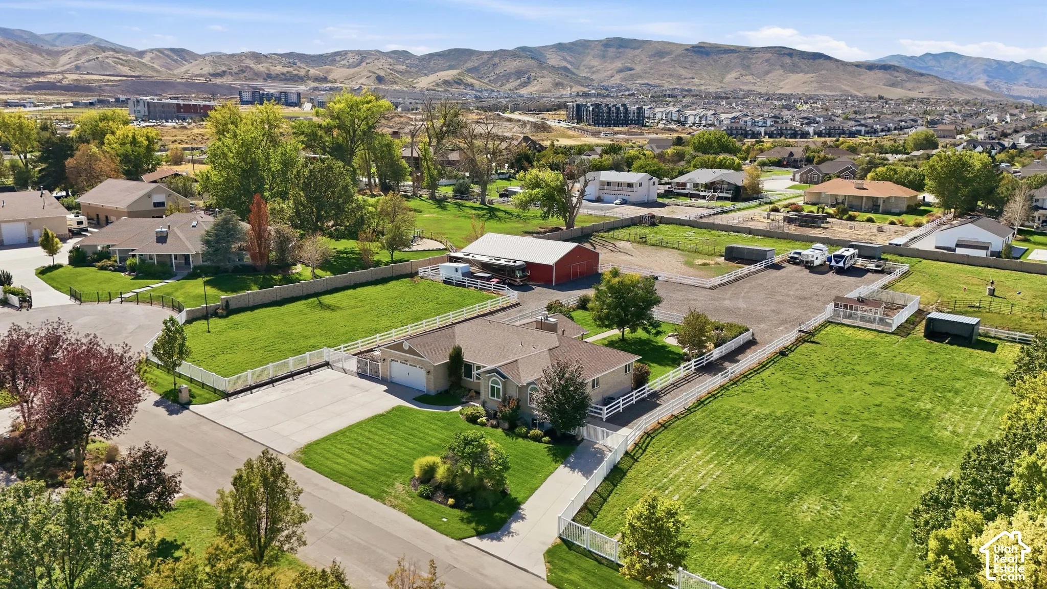 Expansive property featuring a large house with an attached garage, a red barn, a gravel-surfaced area, and multiple fenced grassy sections