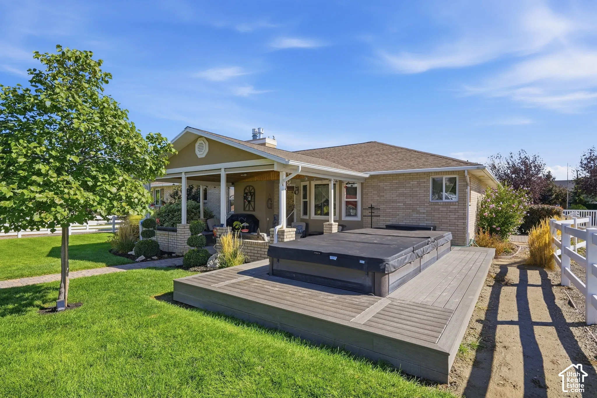 Expansive backyard featuring a large composite deck, covered patio, brick exterior, and white fencing