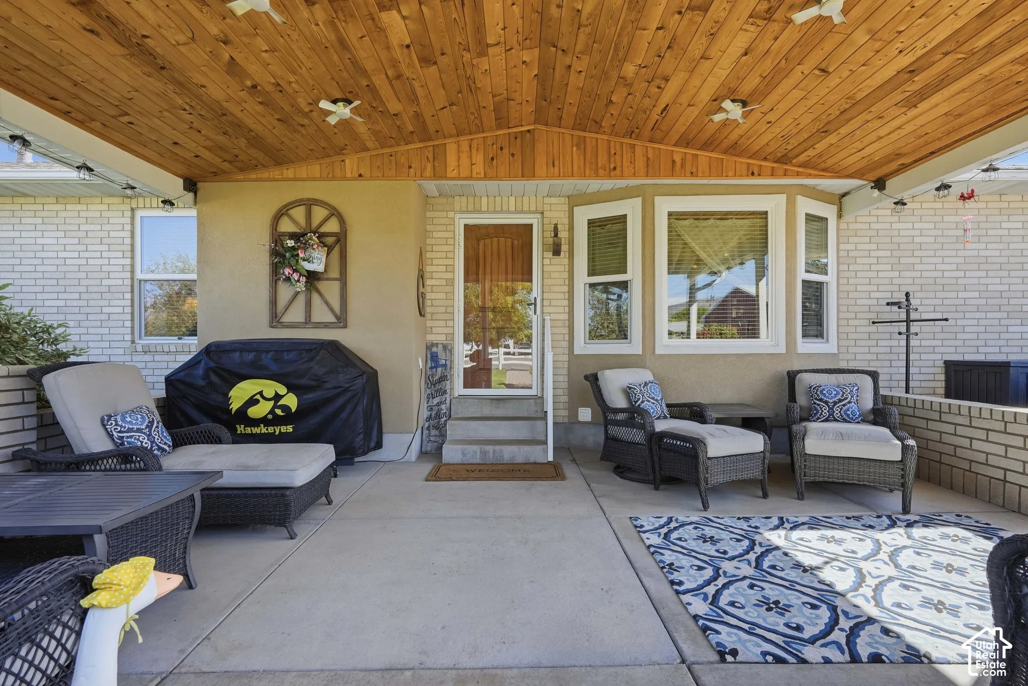 Covered concrete patio with wood-paneled ceiling, exterior brickwork, and bay windows